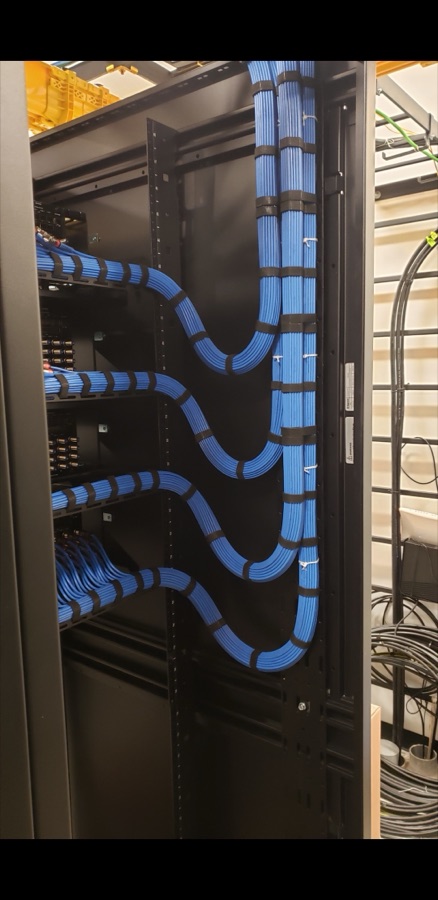 Vertical cable manager with blue Cat 6 cabling routed to labeled patch panels