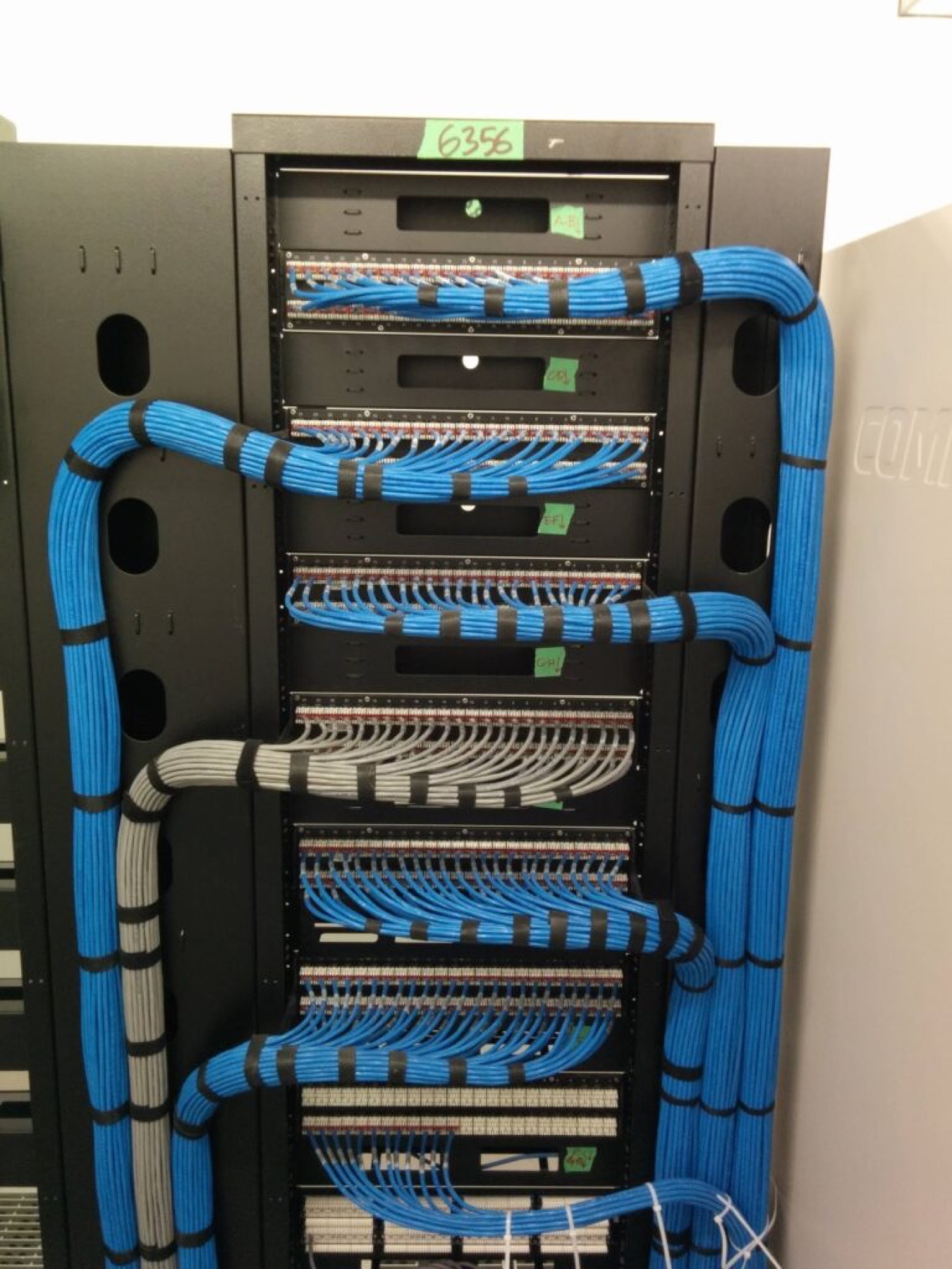Blue Cat 6 cabling dressed into patch panels and routed through a floor-standing rack