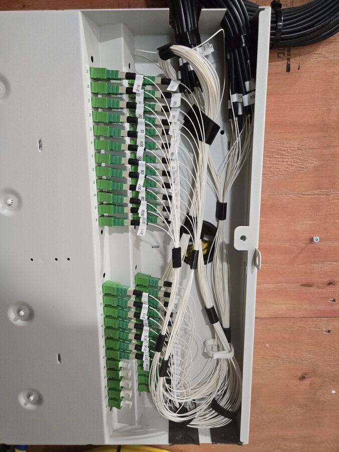 Open fiber distribution cabinet with labeled white fiber leads and green adapters