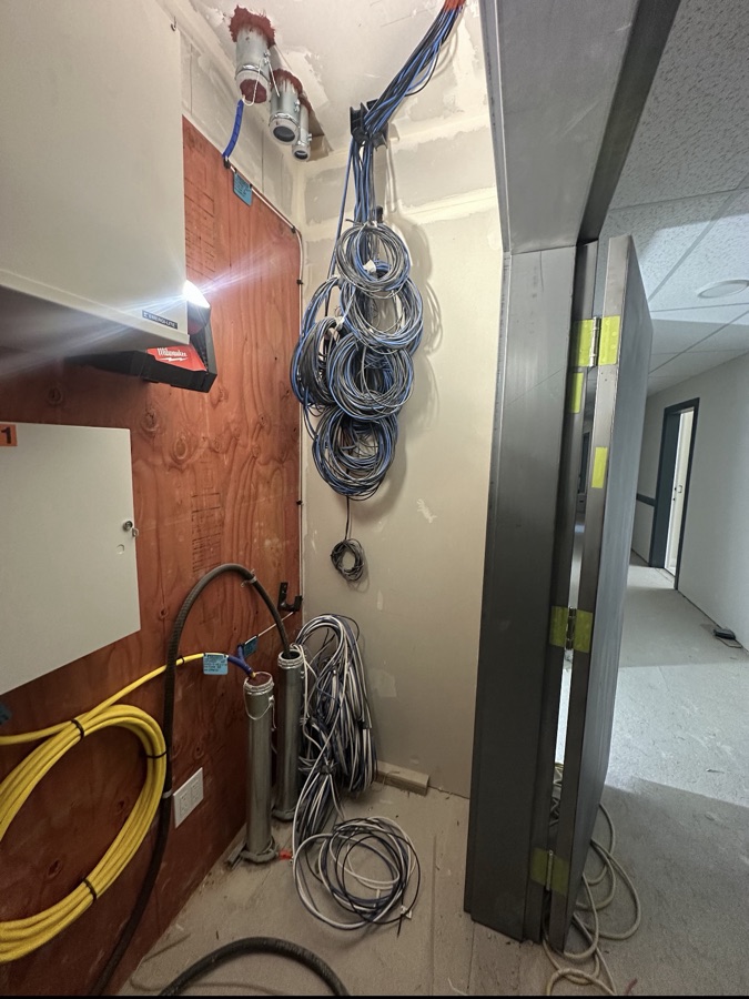 Coiled data cabling and conduit entries arranged on a communications-room wall