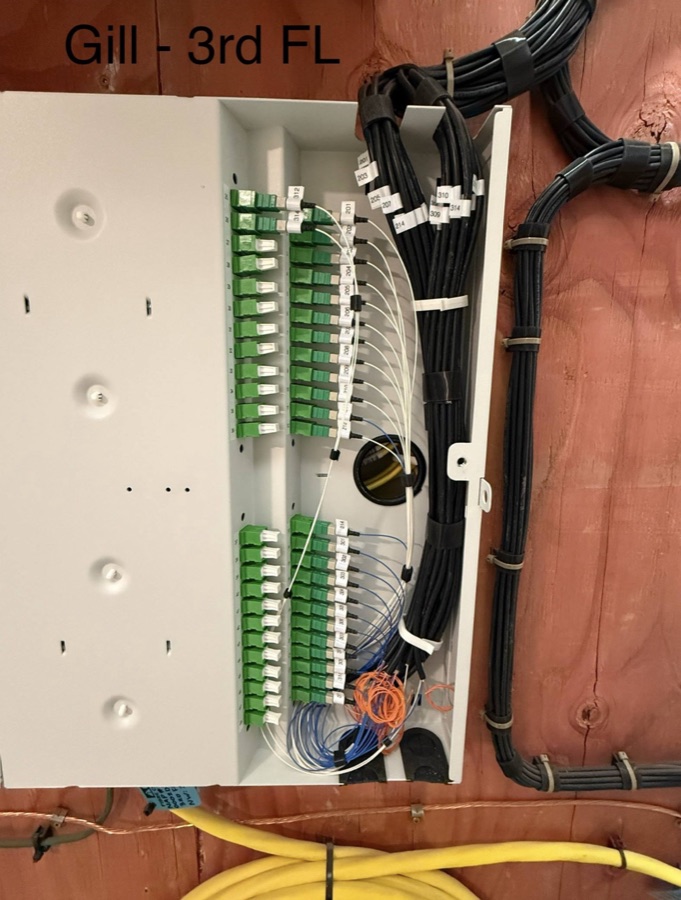 Open distribution cabinet with green fiber adapters and organized orange and black leads