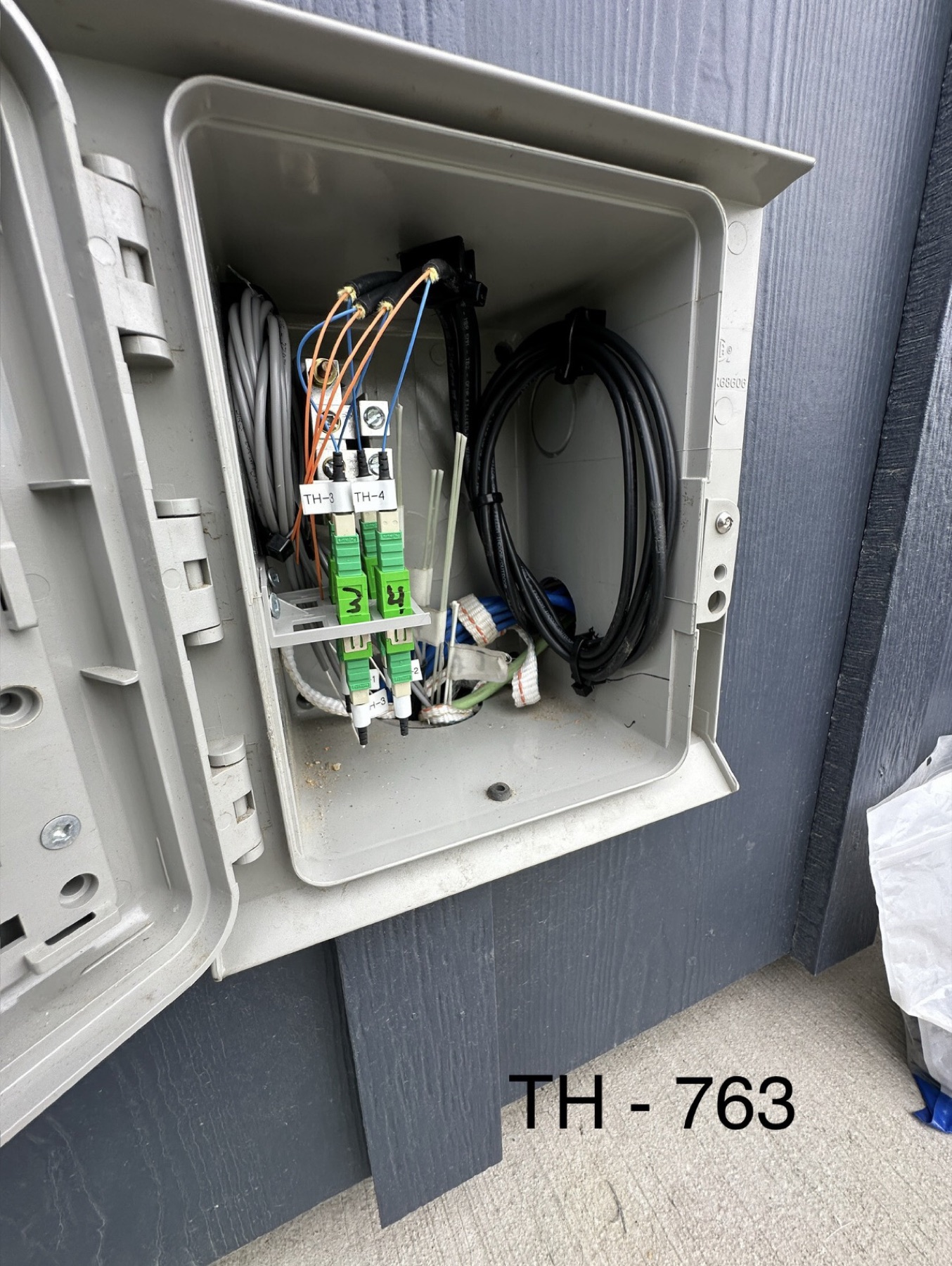 Open exterior fiber service box with paired green adapters and a neatly coiled service cable