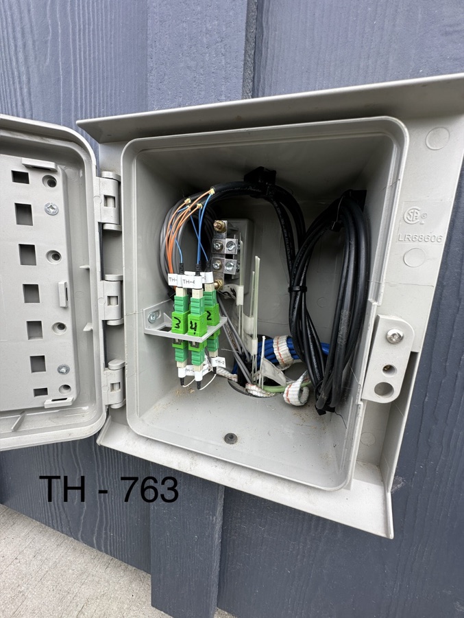 Open exterior service box with green fiber adapters and labeled terminations