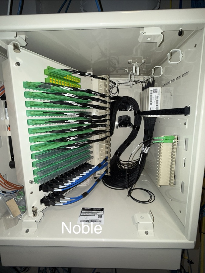 Open fiber distribution cabinet with rows of green adapters and labeled fibers