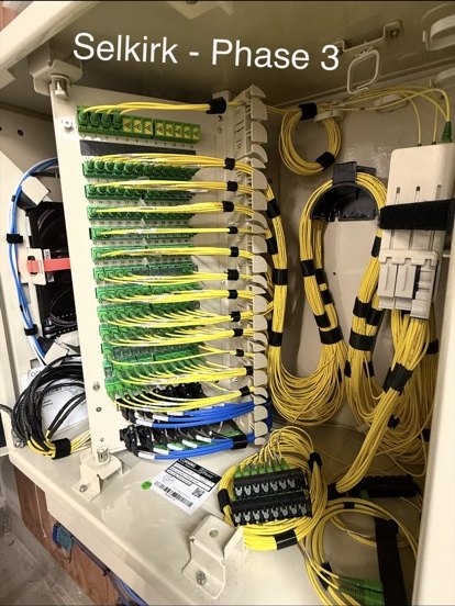 Open fiber distribution cabinet with rows of green adapters and routed yellow patch fibers