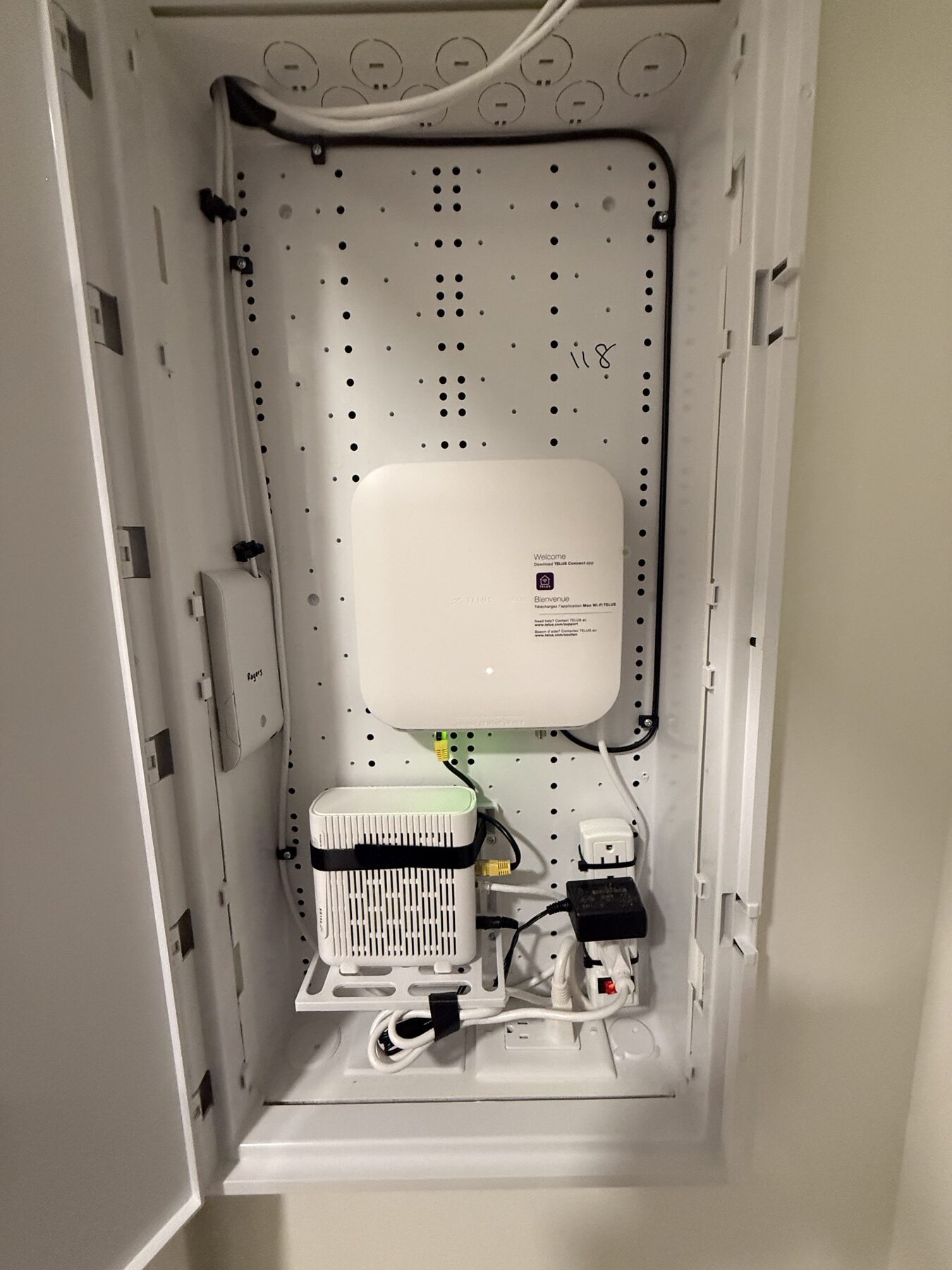 Wall-mounted communications cabinet containing installed network equipment and routed cabling